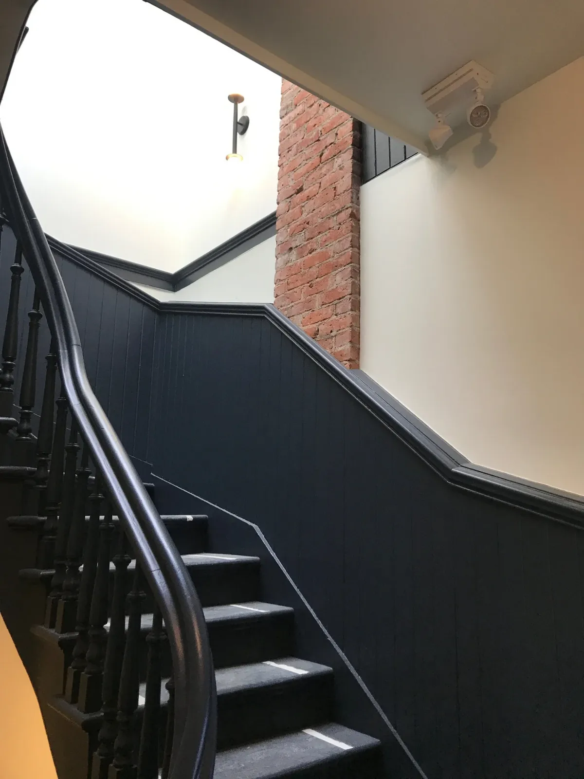 The staircase, black handrails against dark panelling and brick