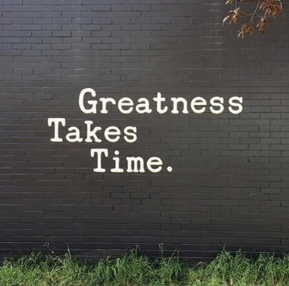 “Greatness Takes Time” painted on the black brick exterior