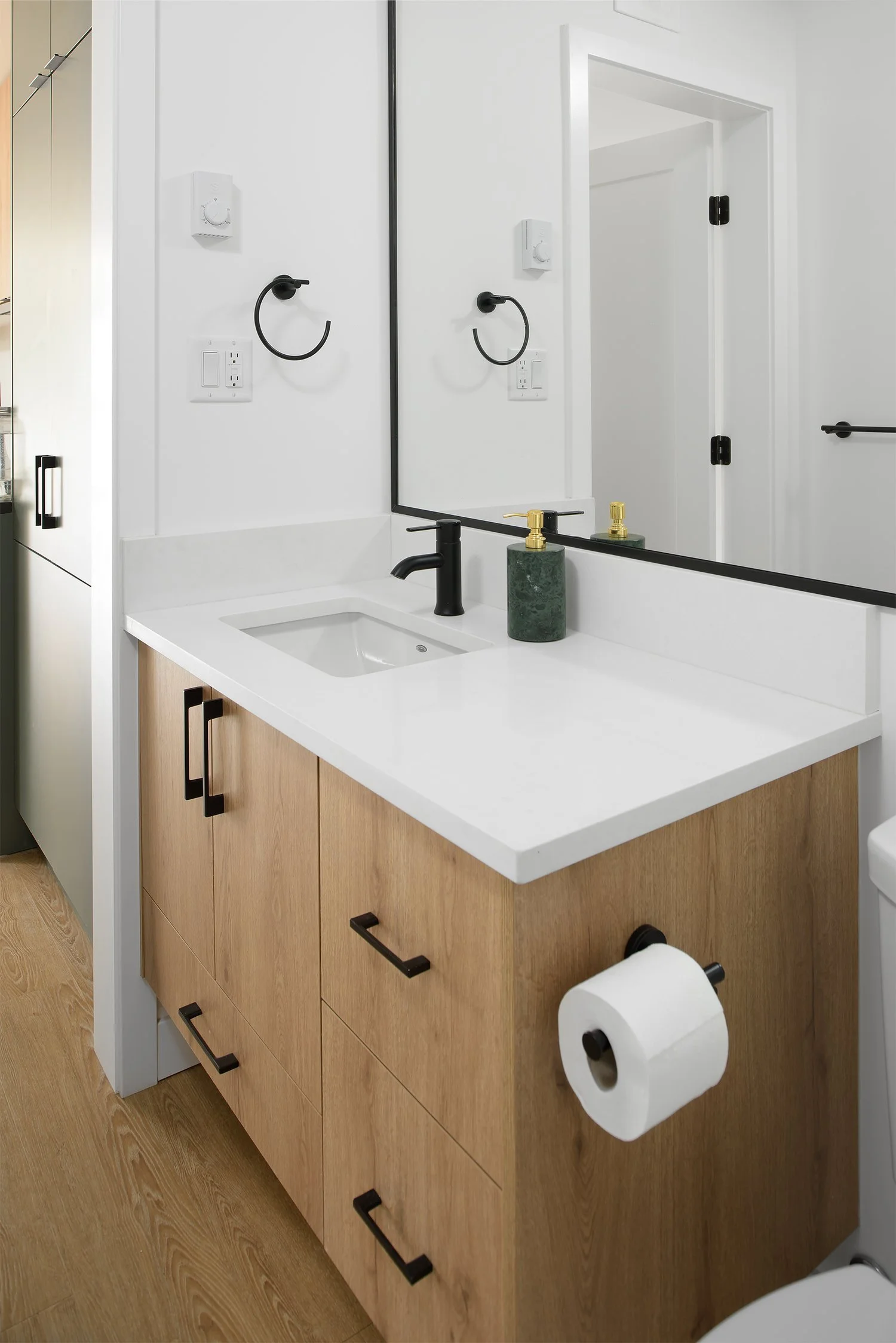 Oak bathroom vanity with black fixtures and a framed mirror