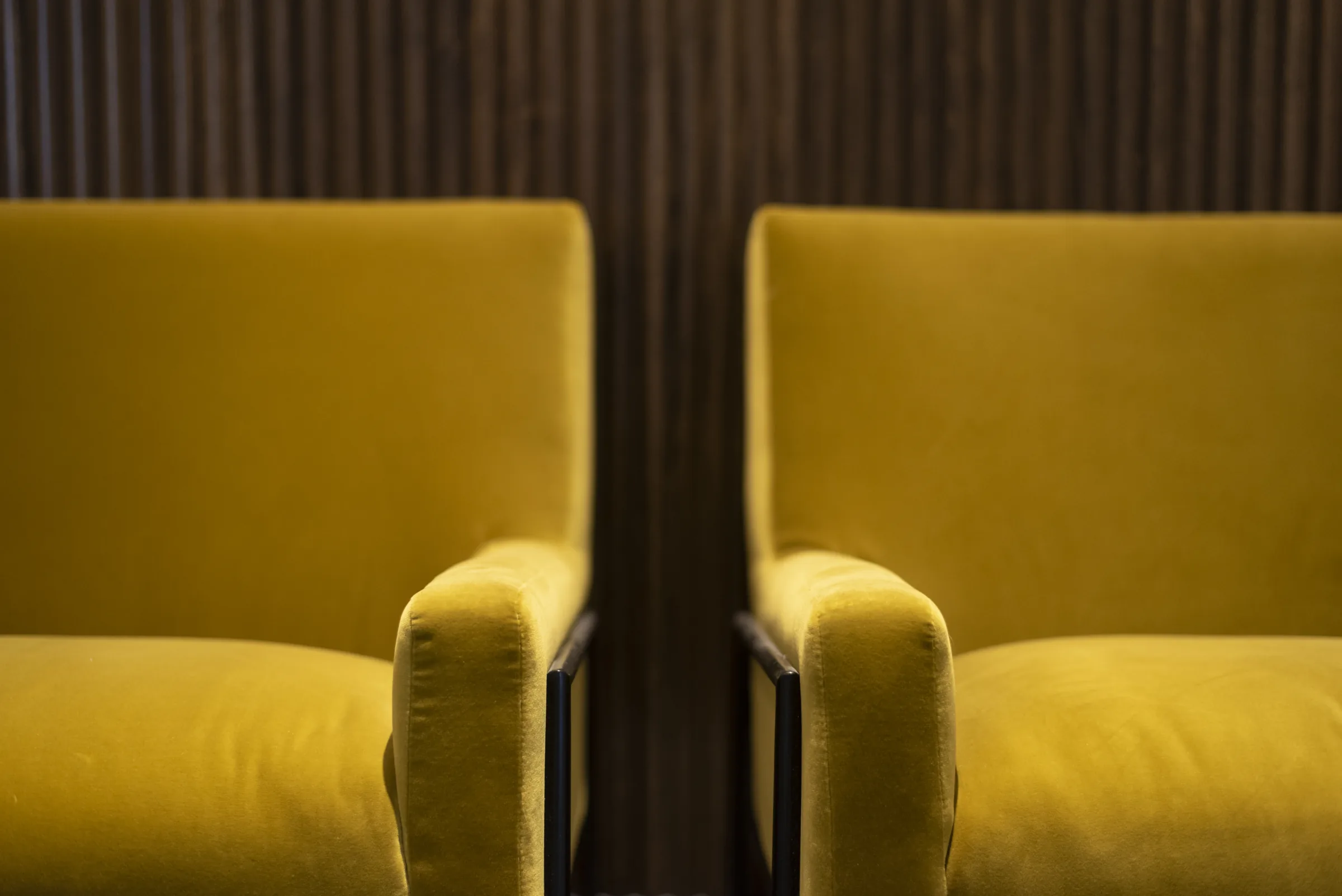 Two mustard velvet armchairs side by side against a dark fluted wood wall