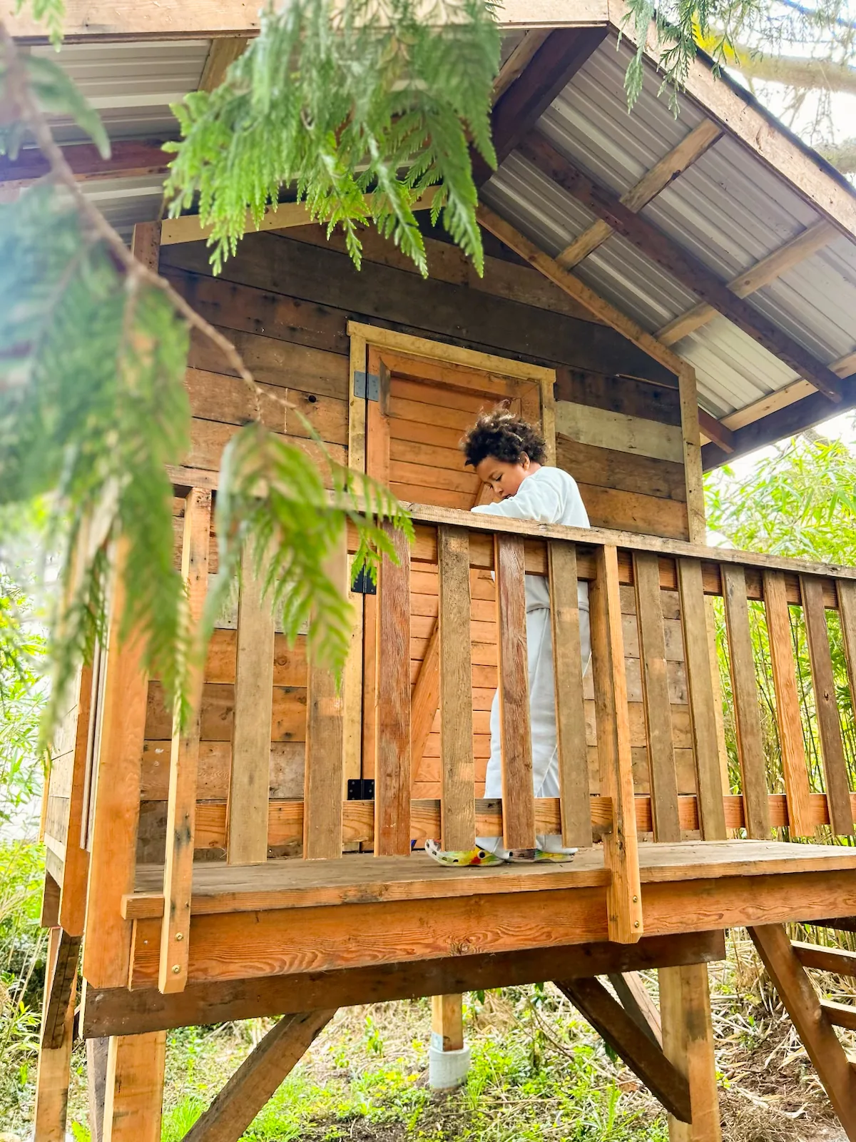 A child on the deck of the playhouse, built from reclaimed boards