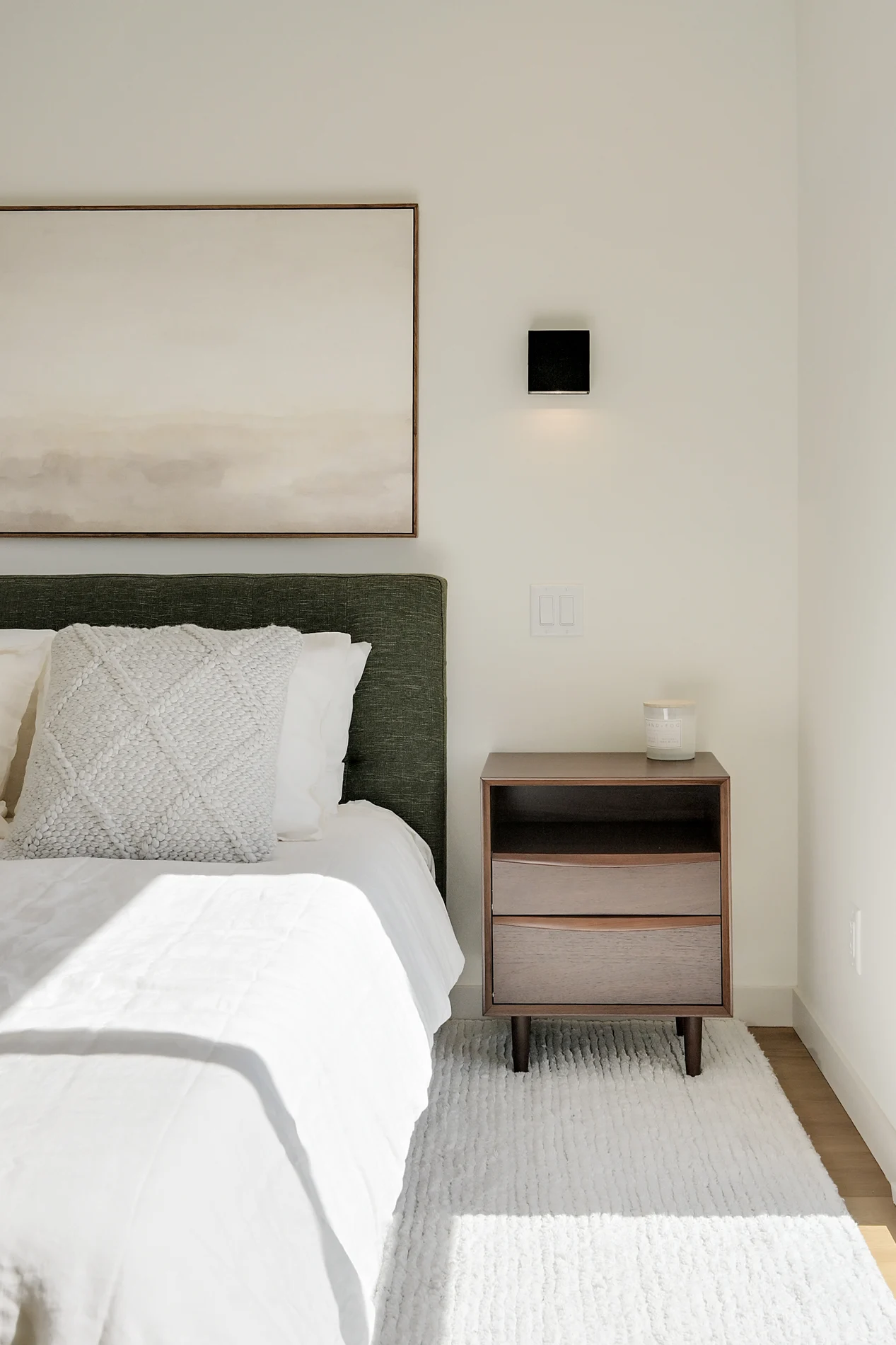 A bedside table beside the bed, under a framed print