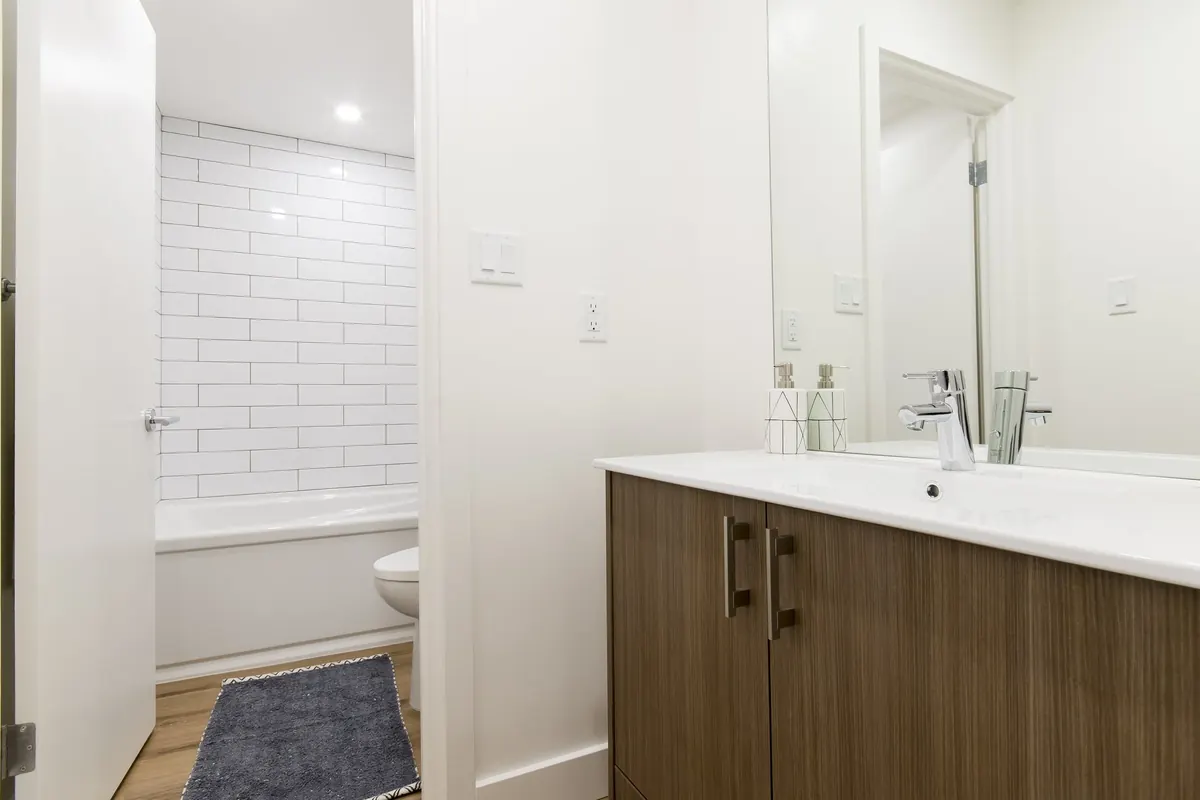 A bathroom with a tiled tub surround and a wood vanity