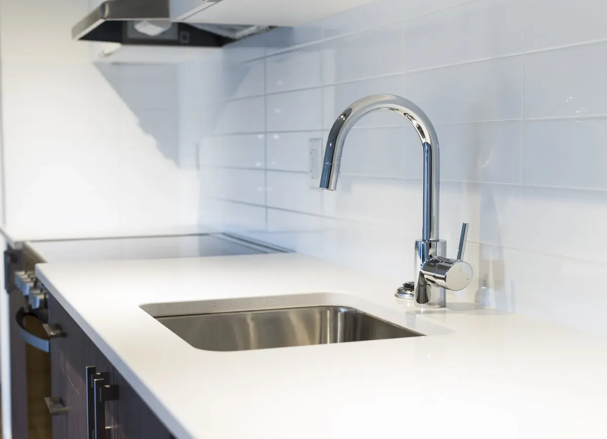 A kitchen sink and quartz counter under the range hood